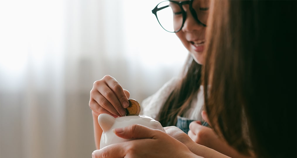 mom and daughter putting coins in a piggy bank