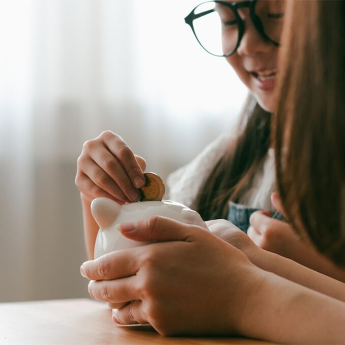 mom and daughter putting coins in a piggy bank