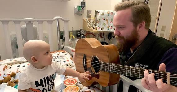 JoyRx Children's Cancer Association-music therapy man with guitar soothing young cancer patient