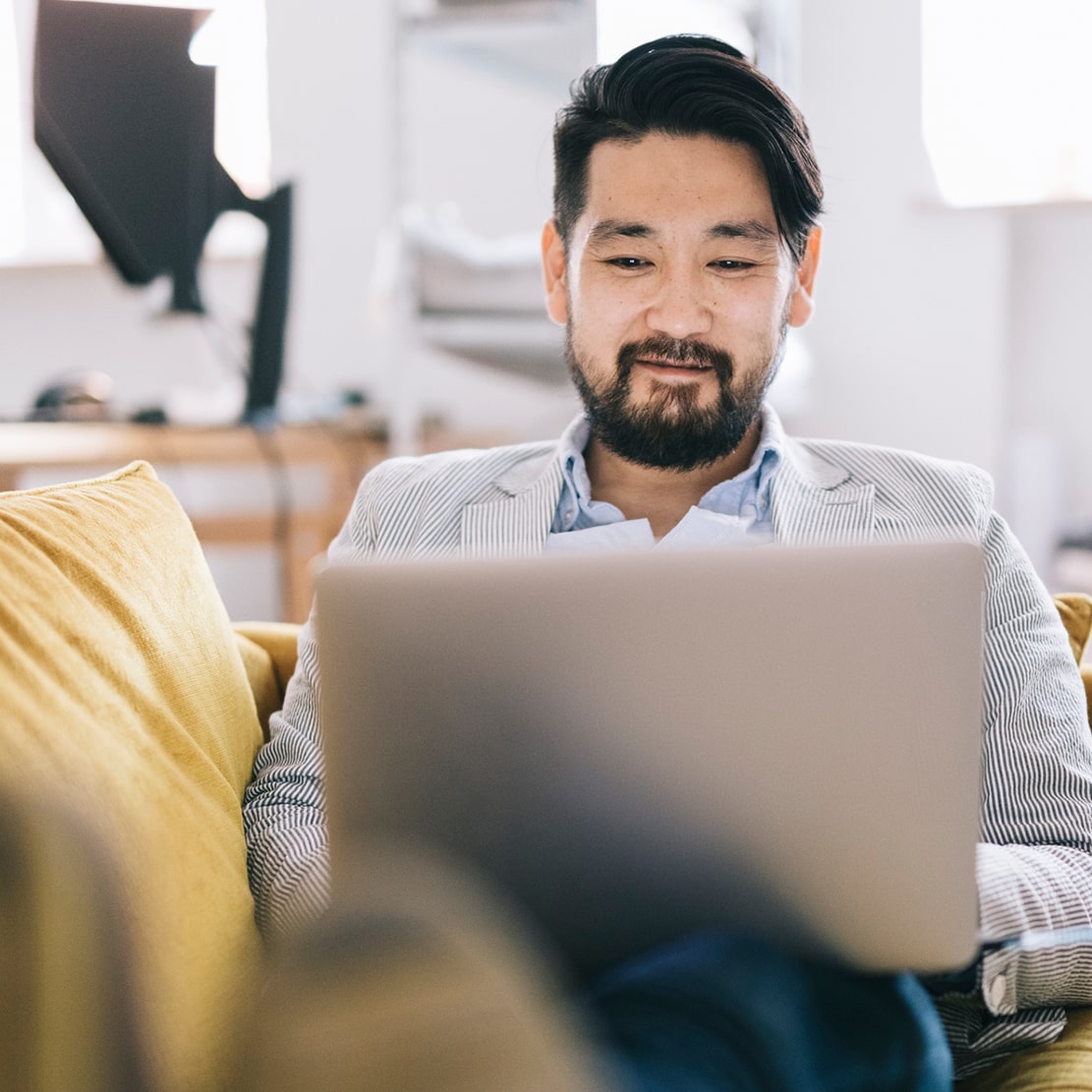 Traits of a Great Financial Advisor-japanese man consideing finances while sitting on yellow couch and typing on computer