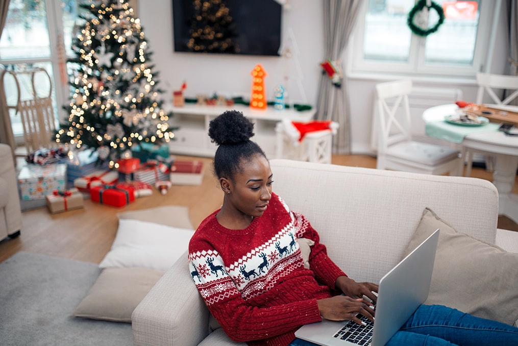 avoid overspending this holiday season-woman using laptop in living room during the holidays