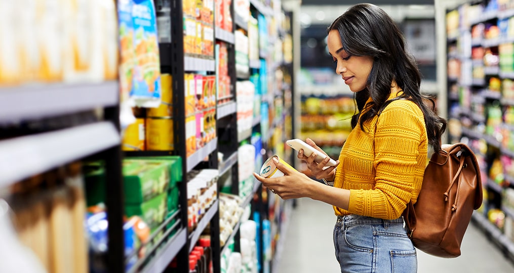 save money on groceries-Woman comparing prices at the grocery store