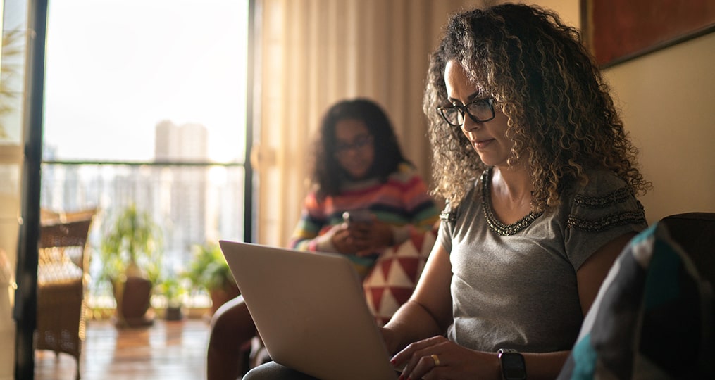 Investing Is Not a Trivial Pursuit_woman searching on her computer while daughter plays on her phone in the background