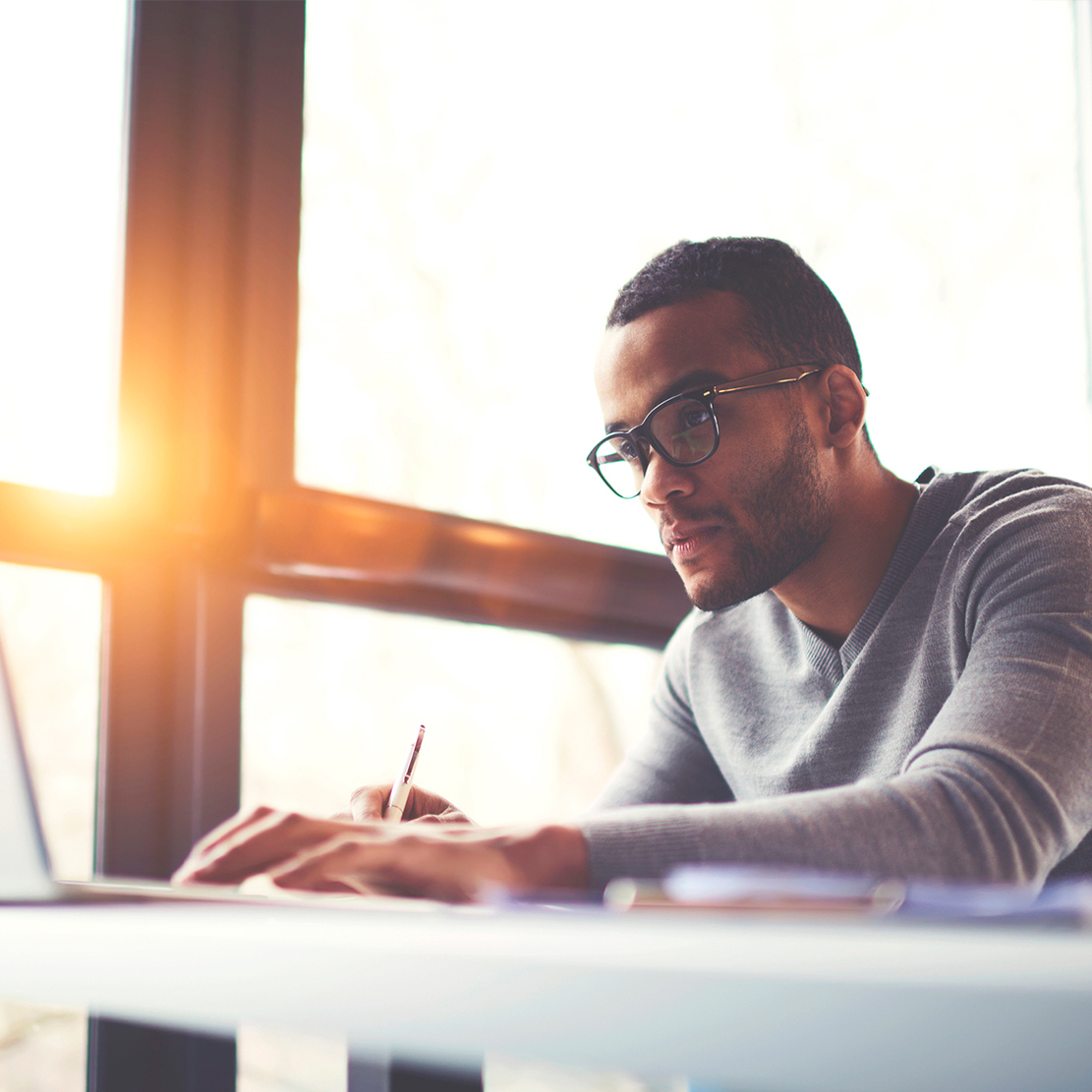 young man working on a computer with the sun shining through the window in the background