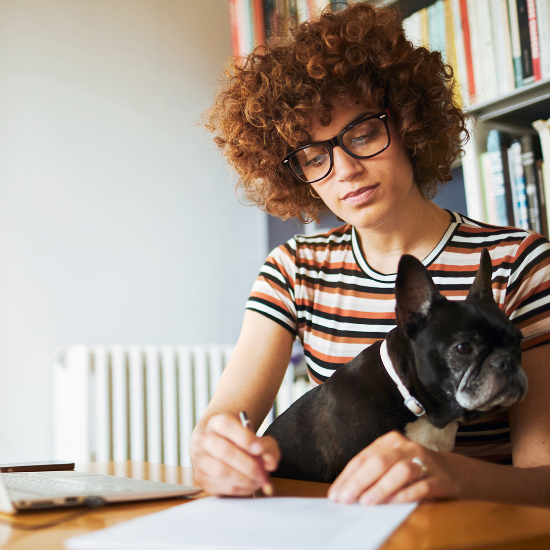 young woman sitting at her desk with her black dog writing on a piece of paper