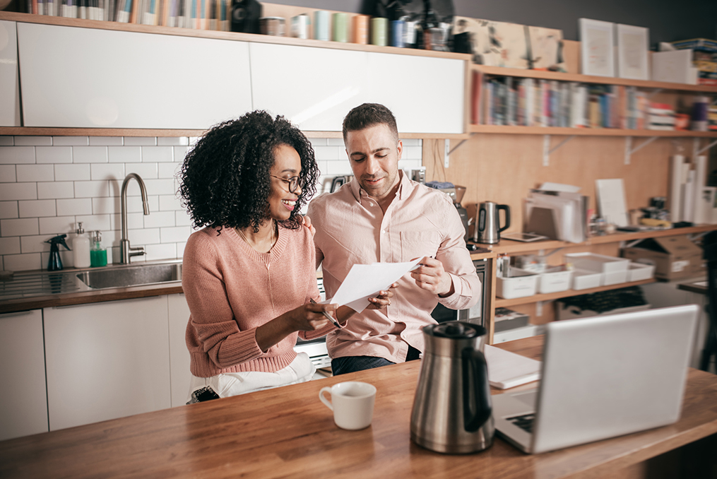 couple sitting in their kitchen looking over paperwork and doing research on a new home purchase