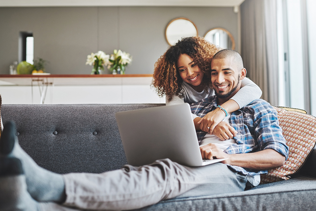 couple smiling on the couch with legs crossed while reviewing their credit report