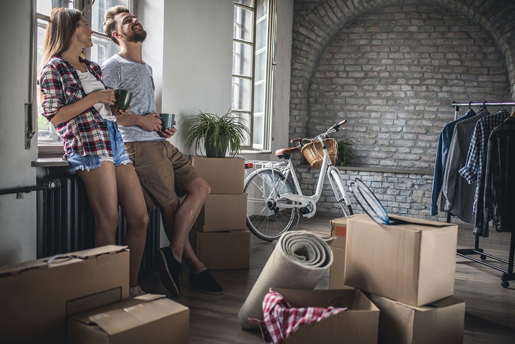 couple standing in their living room surrounded by boxes with a lot of unpacking to do