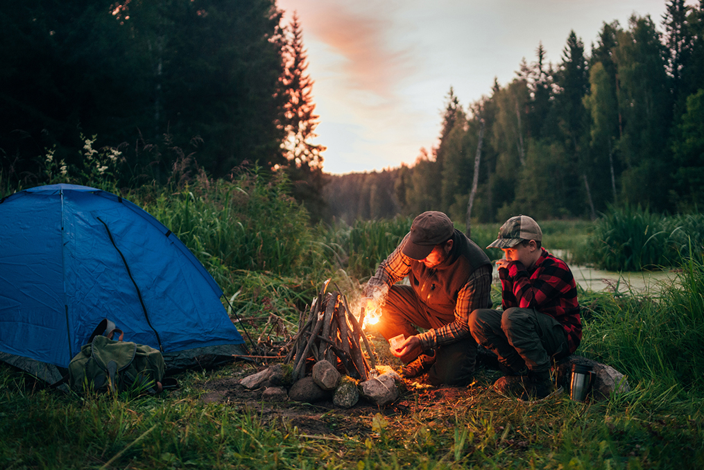 father and son camping trip starting a camp fire near their tent