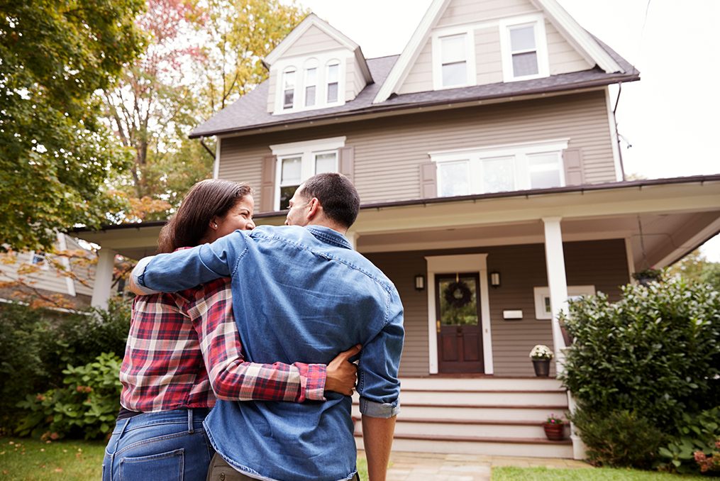 husband and wife hugging each other in front of their new home