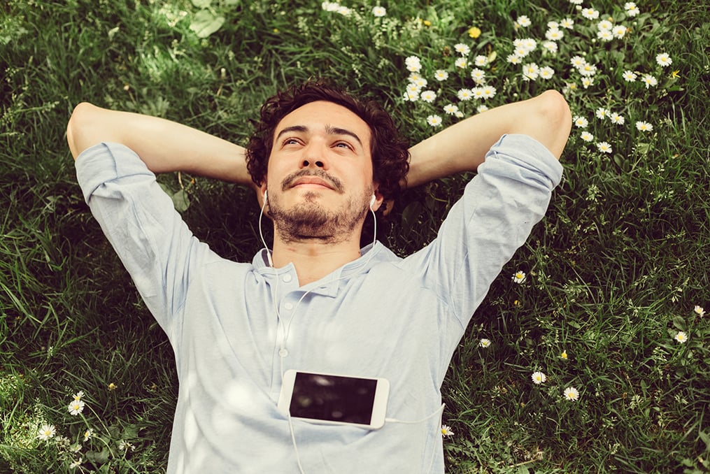 man laying in the grass with his hands behind his back listening to music