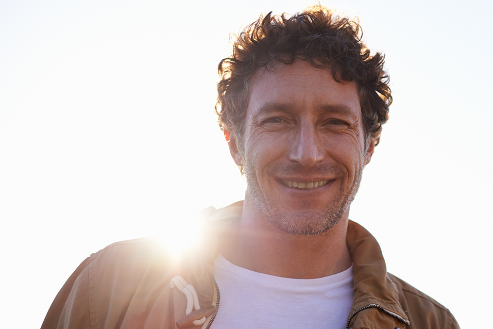 middle age man with facial hair smiling at the camera with the sun shining behind him