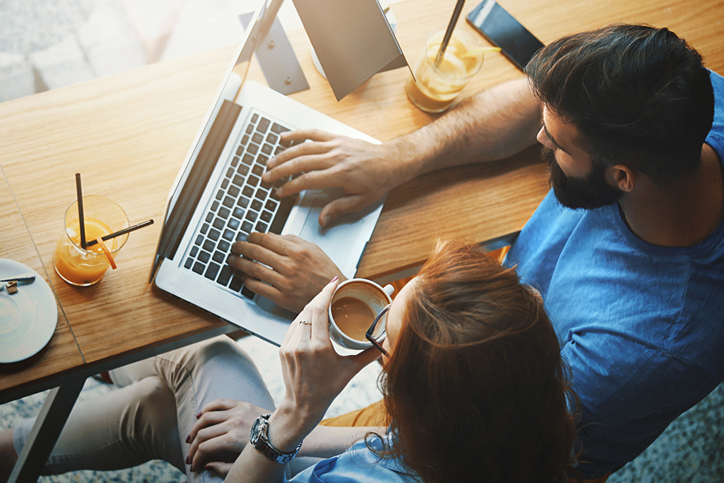 overhead view of a couple sitting at a coffee shop working on a laptop