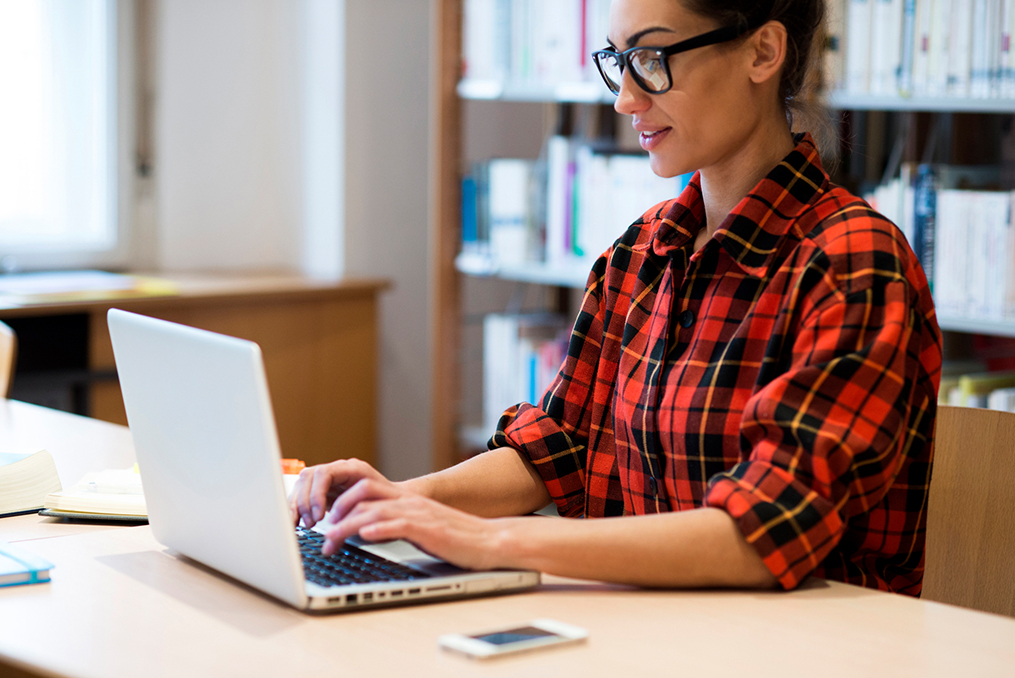 student with glasses typing on her laptop in the school library