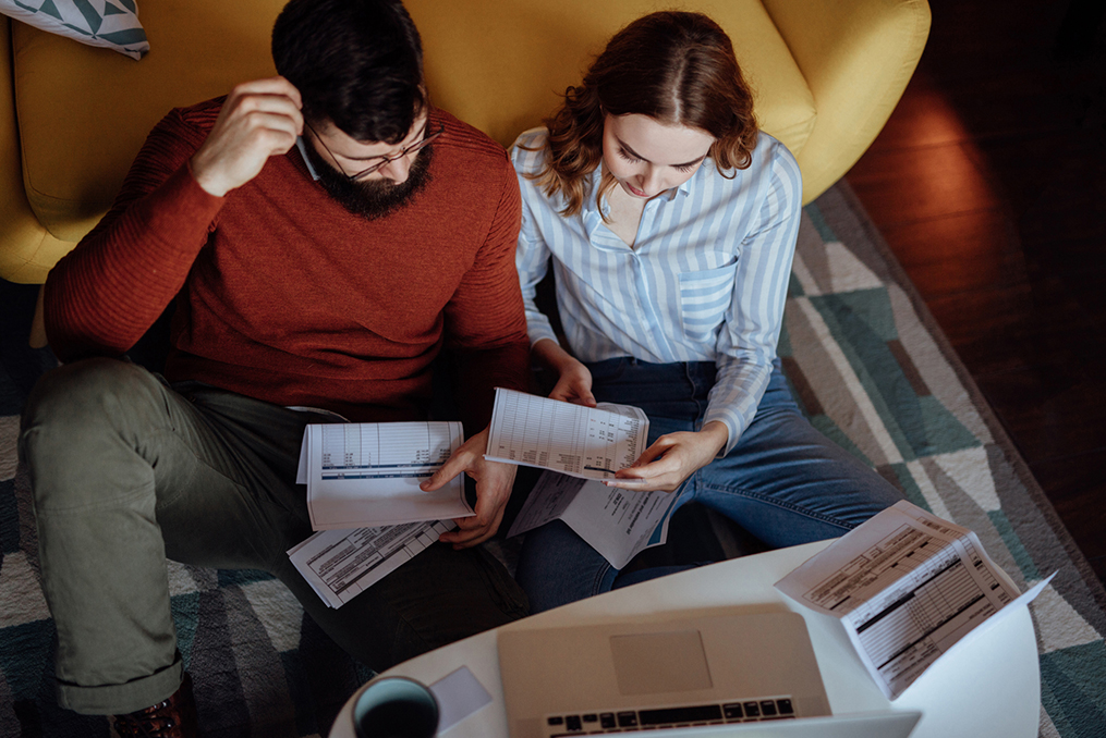 woman and man concentrating on financial documents sitting on the floor in front of their couch