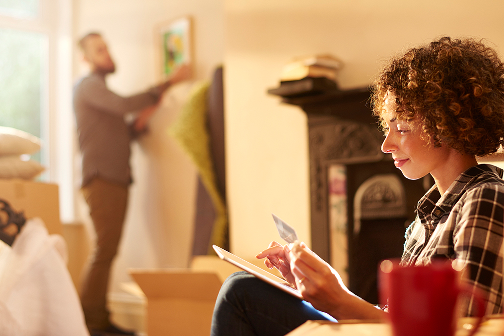 woman making a payment on her tablet while husband hangs a photo in the background