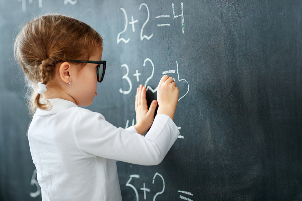 young girl writing math equations on a chalk board