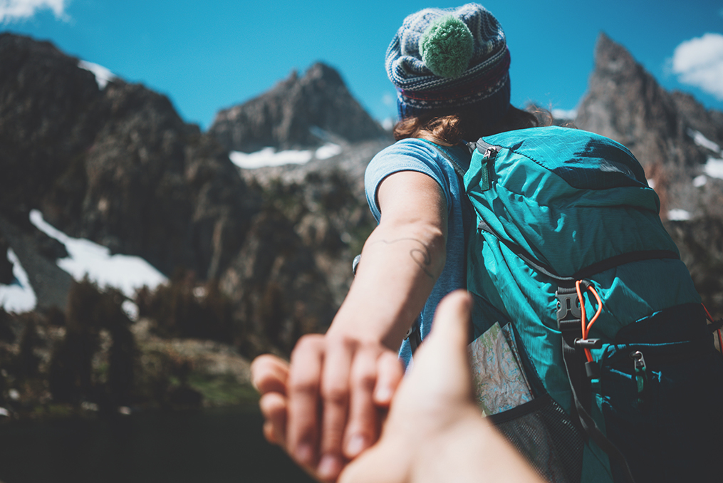 young woman guiding her boyfriend up to the mountain top on a hike