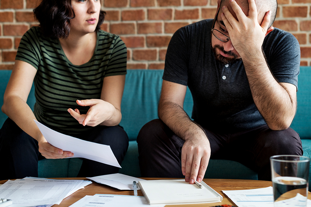 young woman helping her boyfriend with their finances at their coffee table