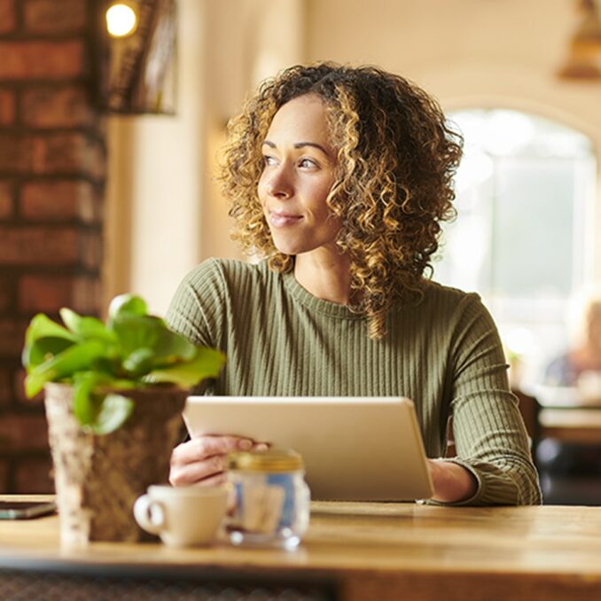 woman looking outside with tablet in hand