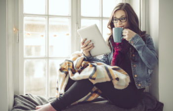 Young woman at home viewing tablet and drinking from a coffee mug.