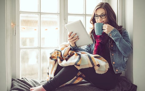Young woman at home reading tablet and drinking from a coffee mug.