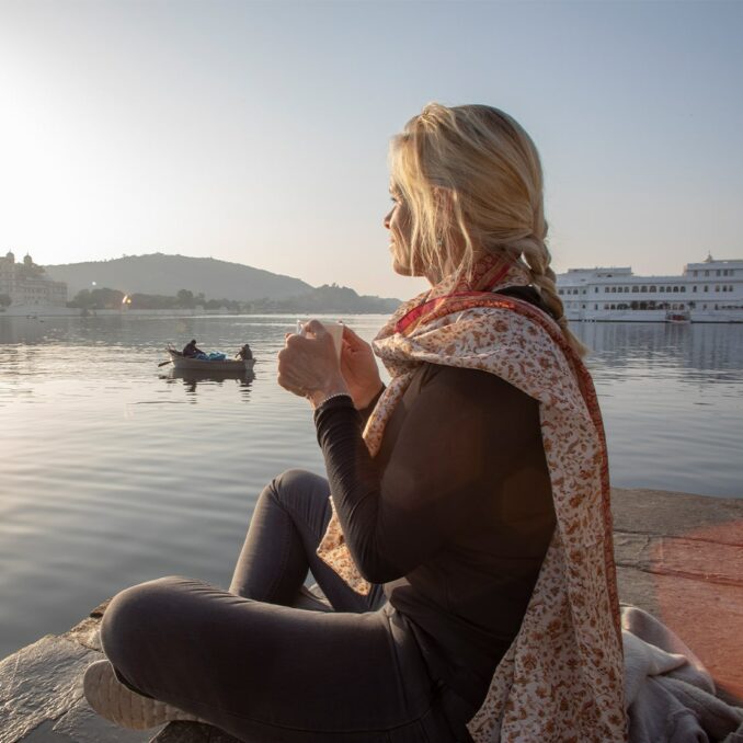 mature woman sits outside looking at the sunset with coffee in her hand