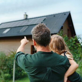 rear view of dad holding a little girl in his arms and showing her a house