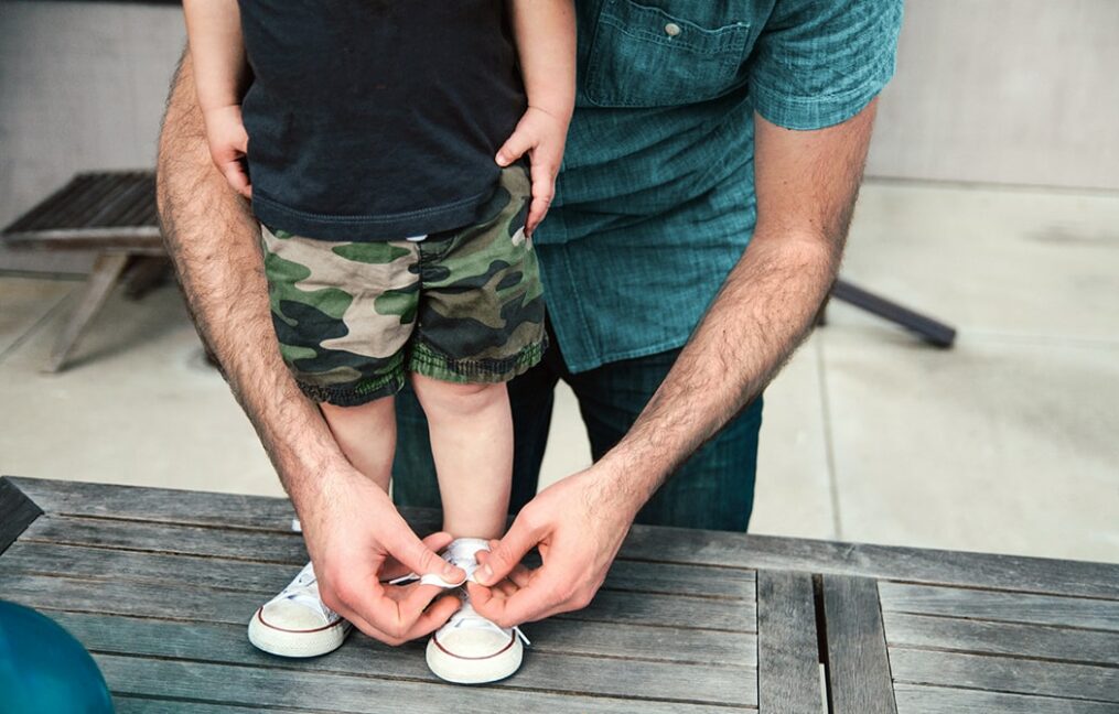 father helping son tie his shoes
