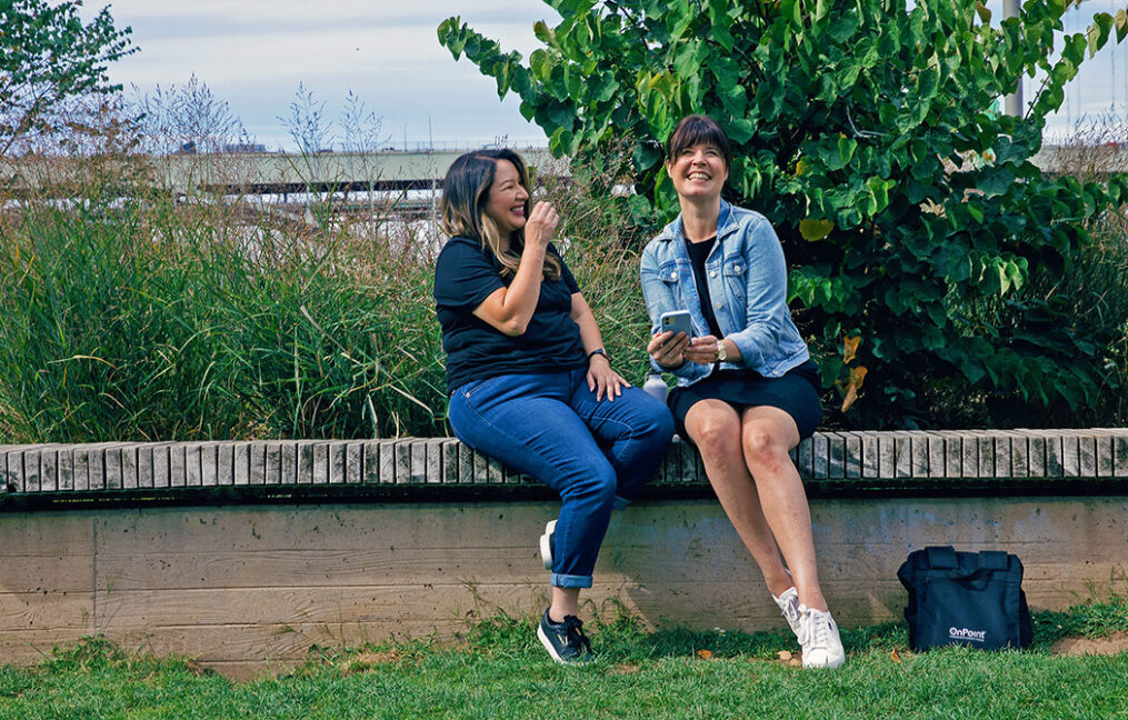 two women sitting in a park laughing with cell phone