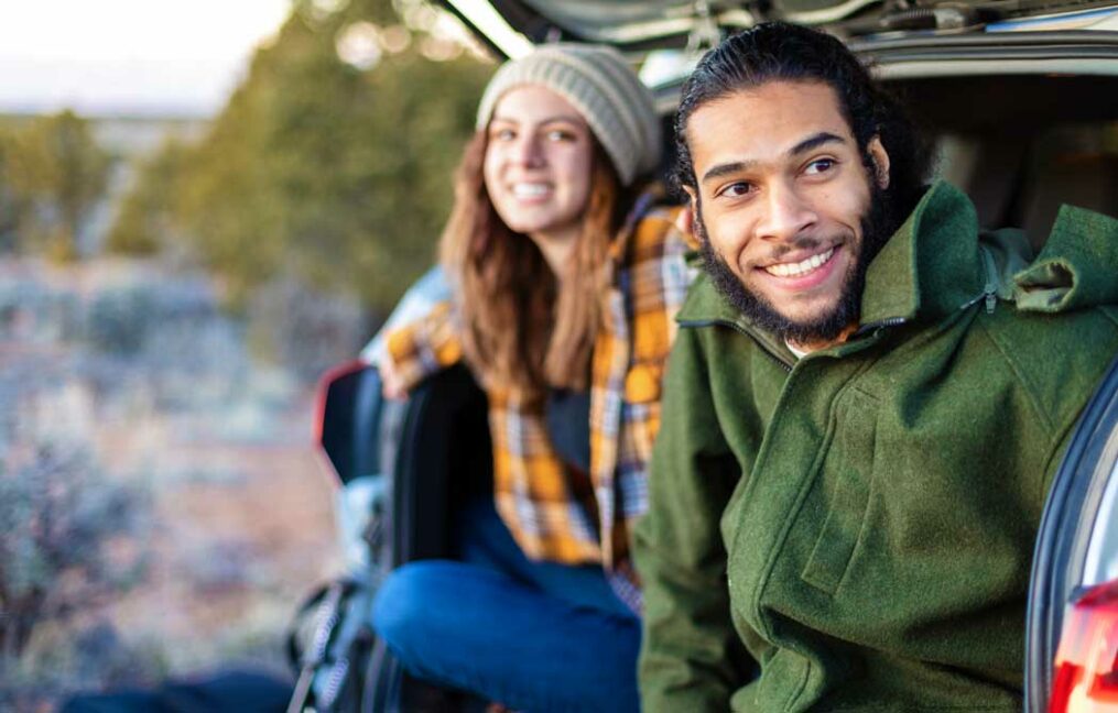 auto loans-man and woman sitting on the back bumper of their SUV near a river in PNW