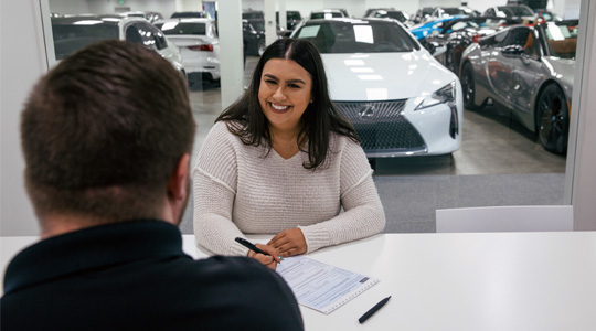 woman sitting at local dealership signing new auto loan papers