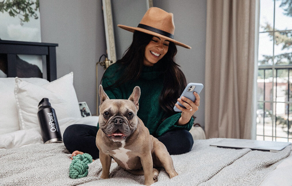 young woman sitting on her bed with her french bull dog exploring onpoint digital banking features