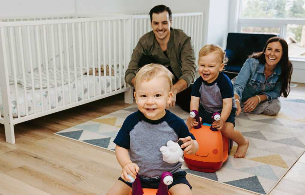 savings accounts-twins toddler boys racing tiny scooters in their room with parents laughing in background