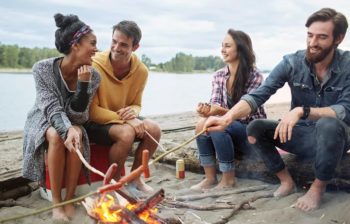 two couples roasting hot dogs over camp fire
