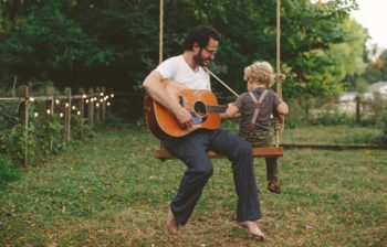 man with guitar sharing swing with child