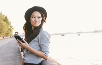 woman in hat by waterfront using phone