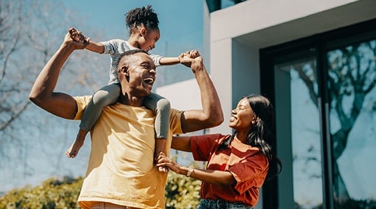 parents giving child piggyback ride in front of house