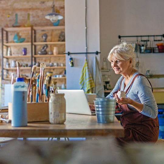 business merchant services-senior business owner working on a laptop in her pottery shop