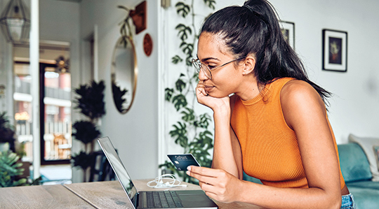woman in home on laptop with OnPoint credit card considering balance transfer