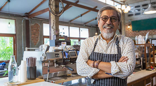 small business local financing-small business owner looking proud behind the counter of their local coffee shop