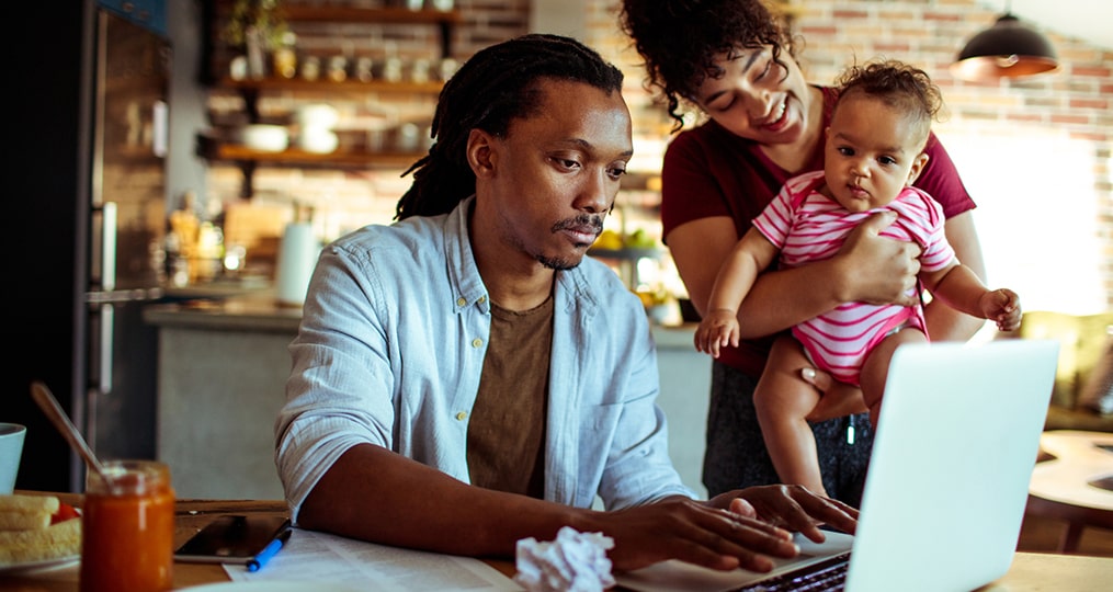 man-woman-and their young child sitting at the dining room table and looking at laptop