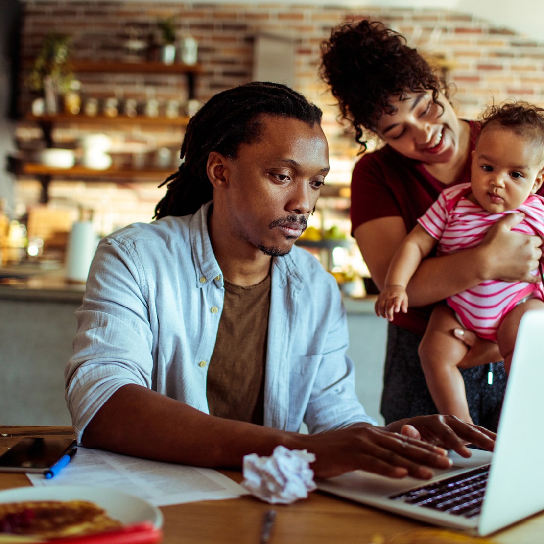 man-woman-and their young child sitting at the dining room table and looking at laptop