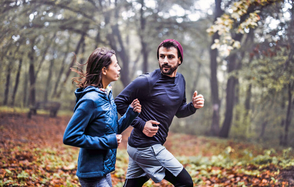 man and woman jogging through forest park in the fall while having a discussion