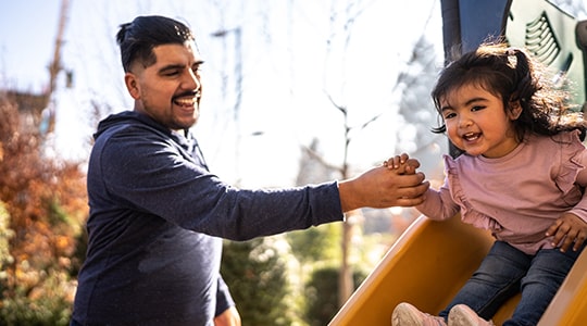 Father helping daughter sliding down the slide in a playground